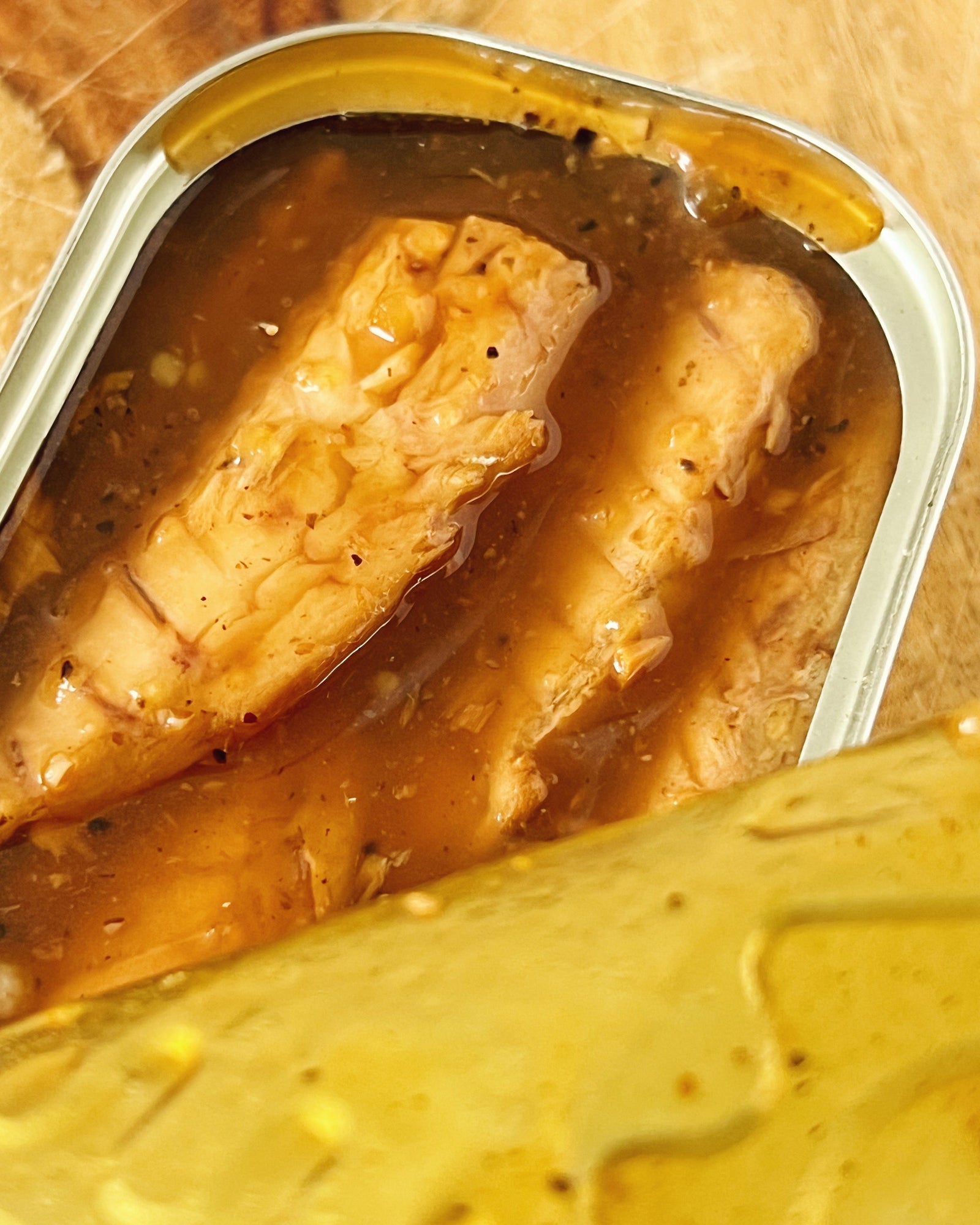 An open tin of Donostia Foods Mackerel Fillets in Harbor Tavern Teriyaki Sauce on a wooden board.