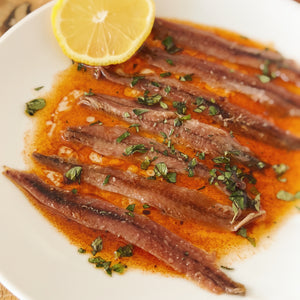 Donostia Foods Cantabrian anchovies in a paprika sauce with oregano and a squeeze of lemon on a white plate.