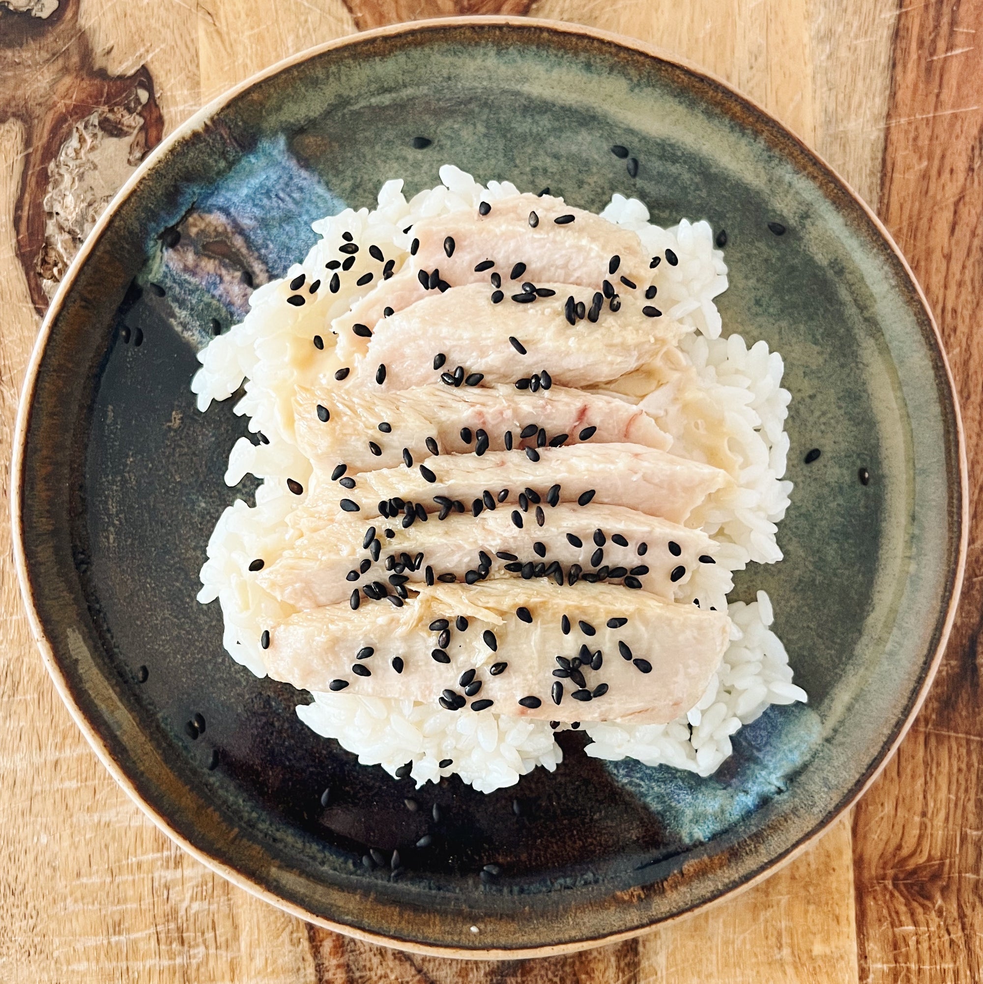 Tuna belly fillets with roasted black sesame seeds on sticky rice served on an artisan ceramic plate.