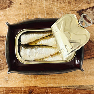 Open tin of sardines in the Donostia Tinned Fish Dish (version #1) on a wooden table.